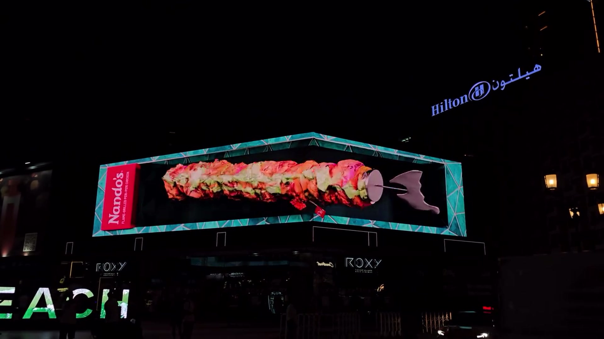 Nando's Espetada chicken skewers emerging from an anamorphic 3D billboard at night